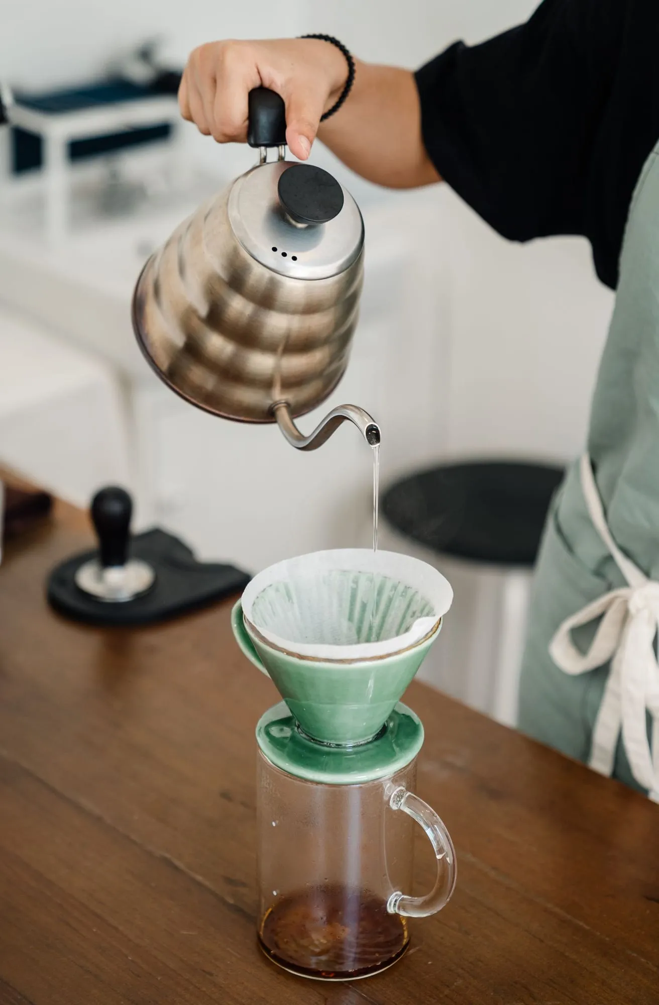 Mână care toarnă apă dintr-un ceainic peste filtrul de hârtie dintr-un dripper ceramic verde